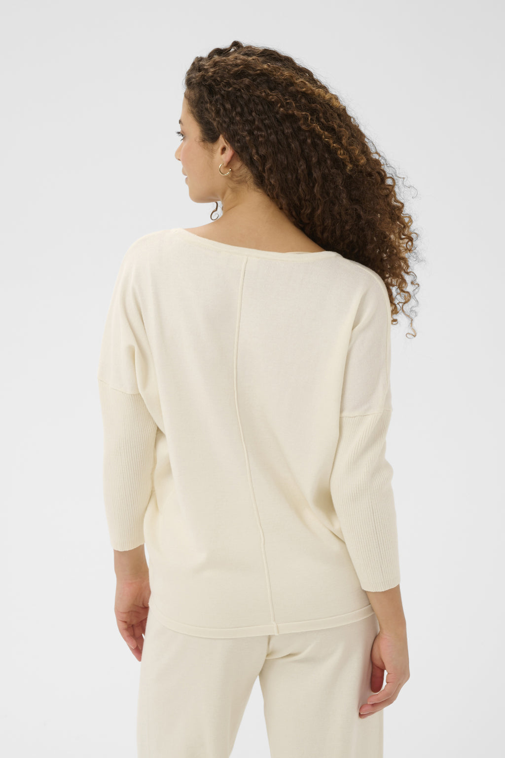 Woman wearing a cream-colored sweater and pants on a light gray background