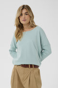 Woman wearing a light blue sweater and beige pants on a white background