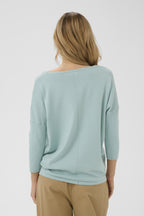 Woman wearing a light blue sweater and beige pants on a white background