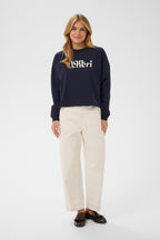 Woman wearing a navy sweater with a brand logo on a white background