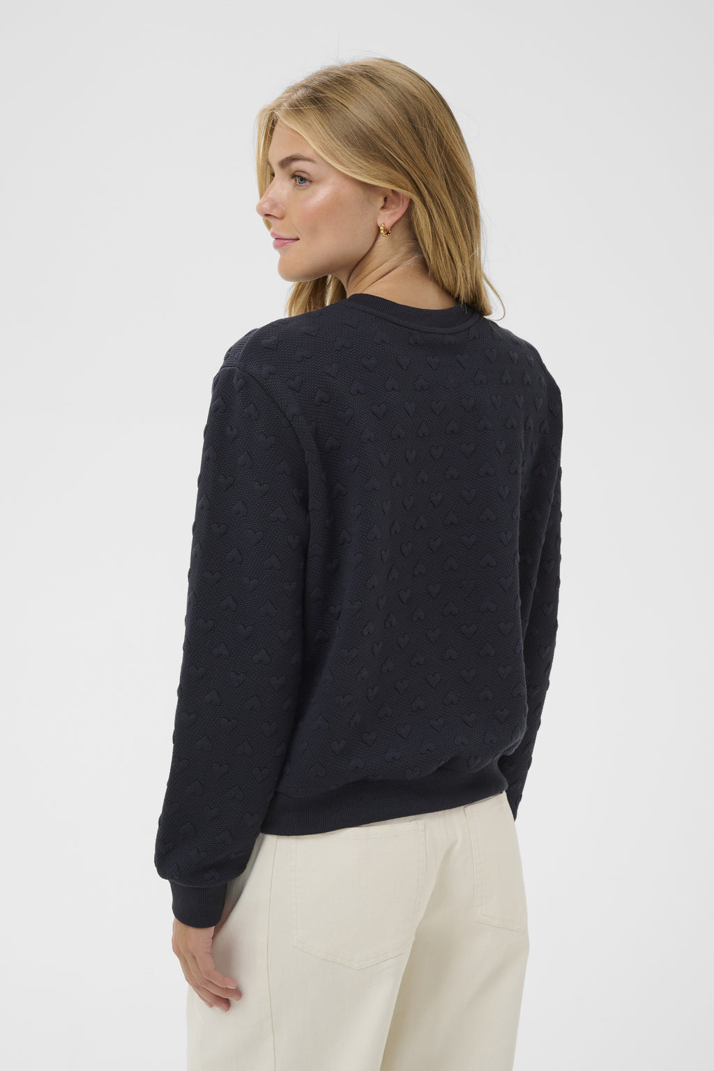 Woman wearing a dark blue sweater and light-colored pants on a white background