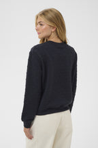 Woman wearing a dark blue sweater and light-colored pants on a white background