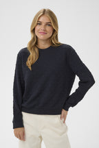 Woman wearing a dark blue sweater and white pants on a light gray background