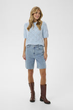Woman wearing a light blue sweater, denim shorts, and brown boots on a white background
