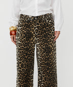 Person wearing leopard print pants with a white shirt on a plain background