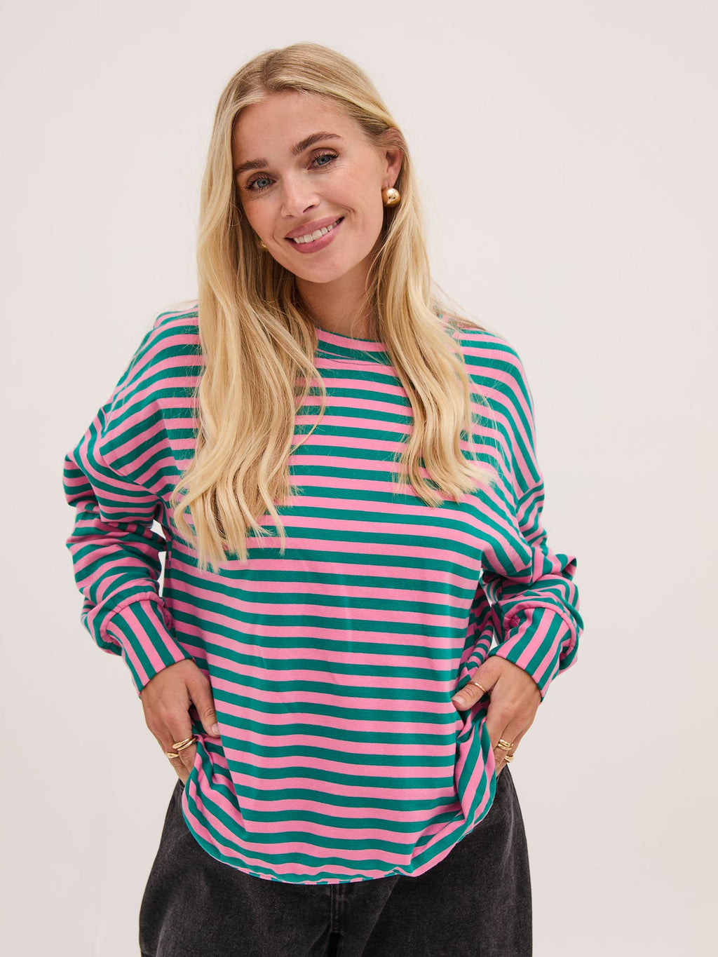 Woman wearing a striped shirt with pink and green horizontal stripes on a plain background