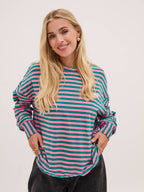 Woman wearing a striped shirt with pink and green horizontal stripes on a plain background